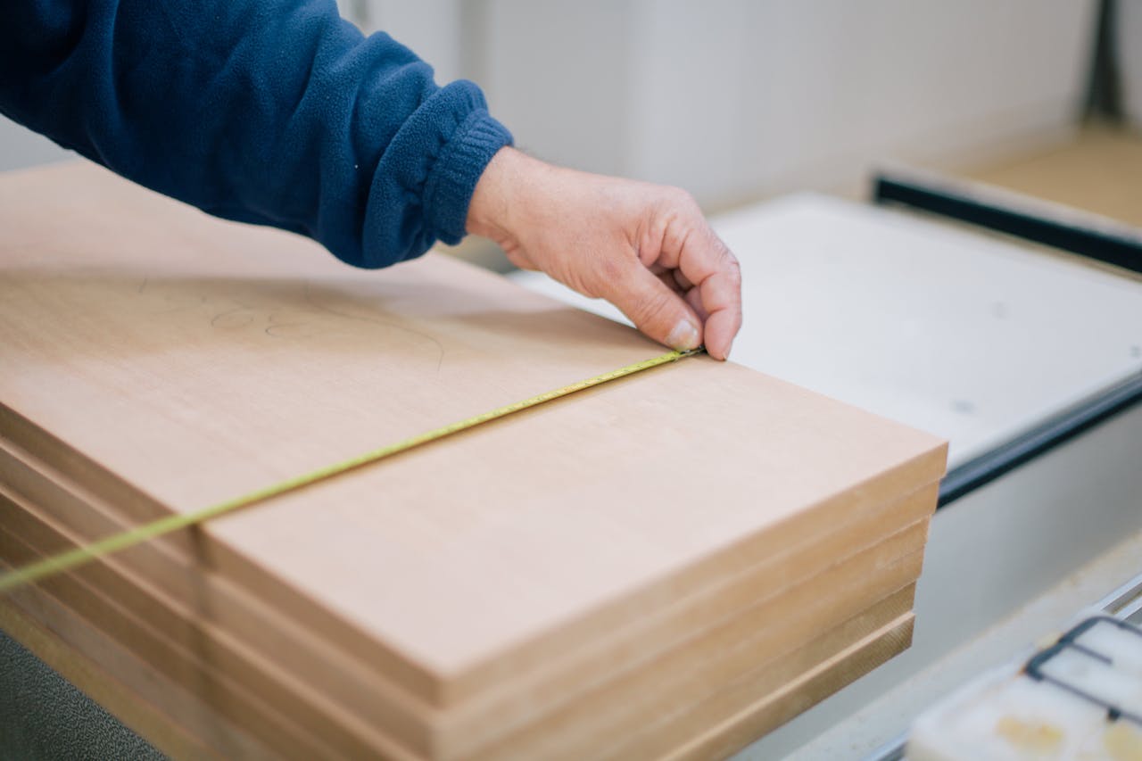 Close-up of a carpenter's hand using a tape measure to measure wooden planks indoors.