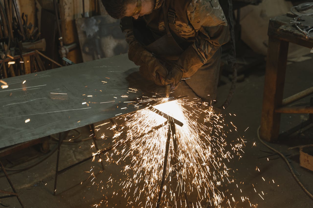 A professional welder cutting metal in an industrial workshop with bright sparks flying around.