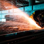 An industrial worker using an angle grinder to cut steel, creating bright sparks in a factory setting.
