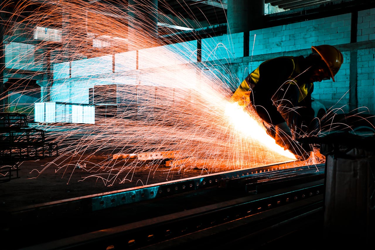An industrial worker using an angle grinder to cut steel, creating bright sparks in a factory setting.